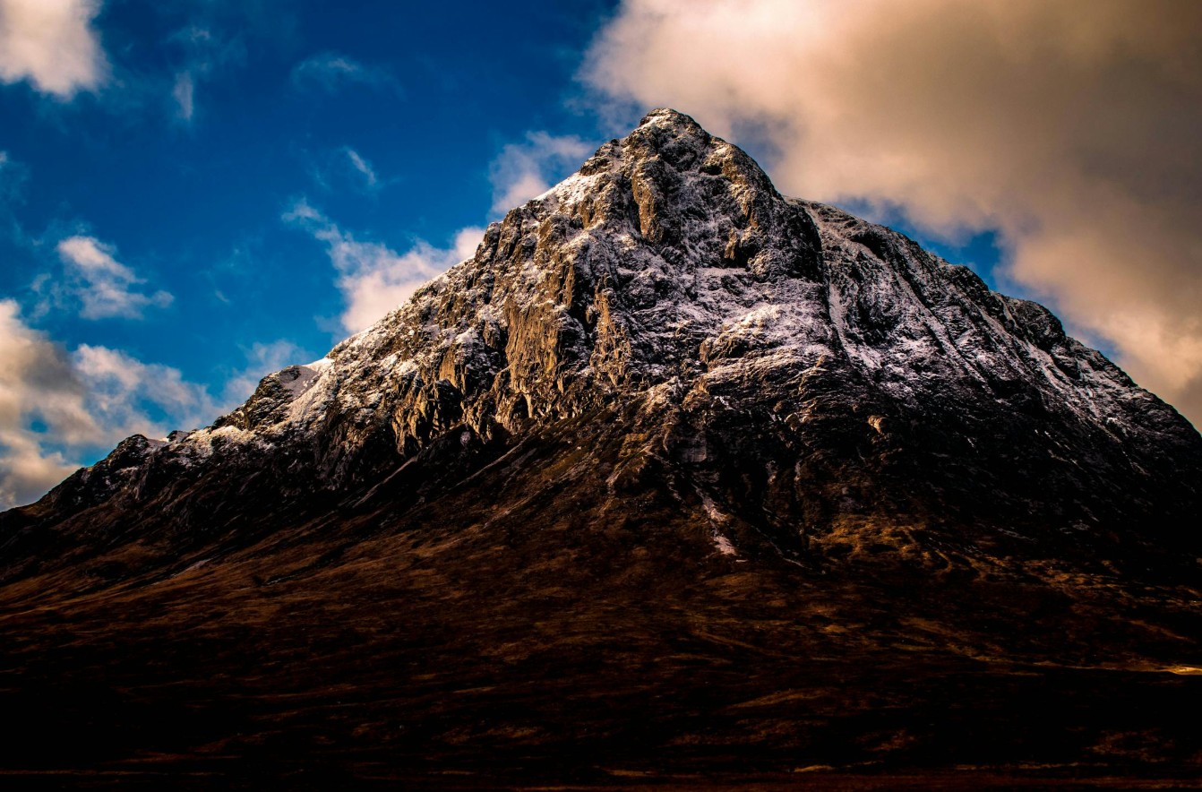 Dramatic view of the snow-capped Buachaille Etive Mòr in Glencoe, Scotland under a bright sky.